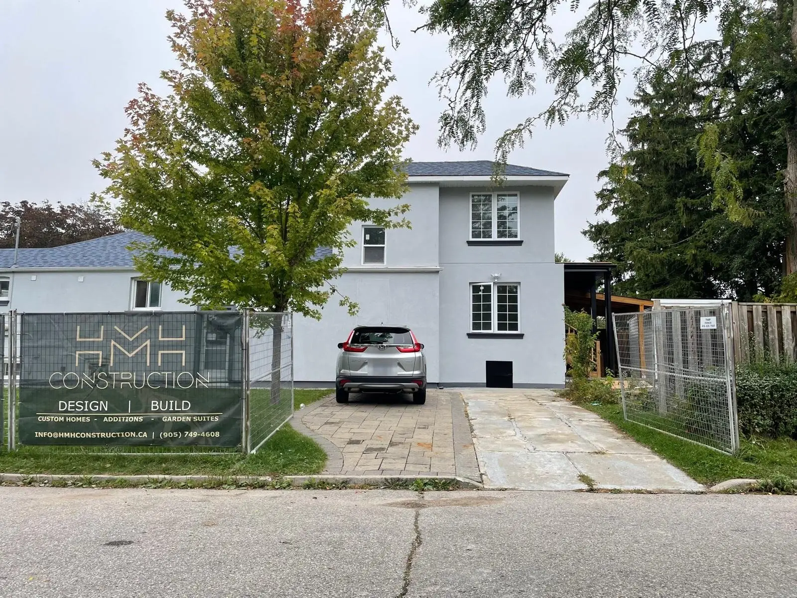 The finished two-storey home from the street, stucco exterior with black trim and a new driveway