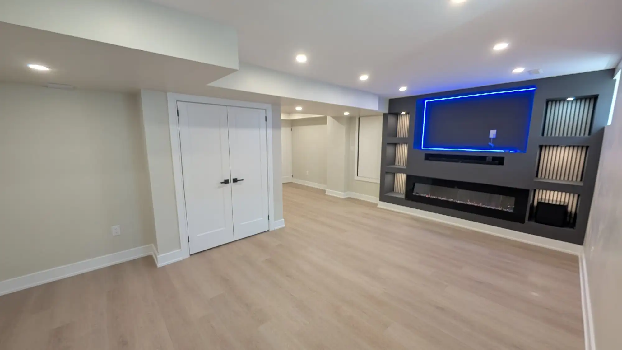 A finished basement rec room with a built-in media wall, linear fireplace and integrated lighting