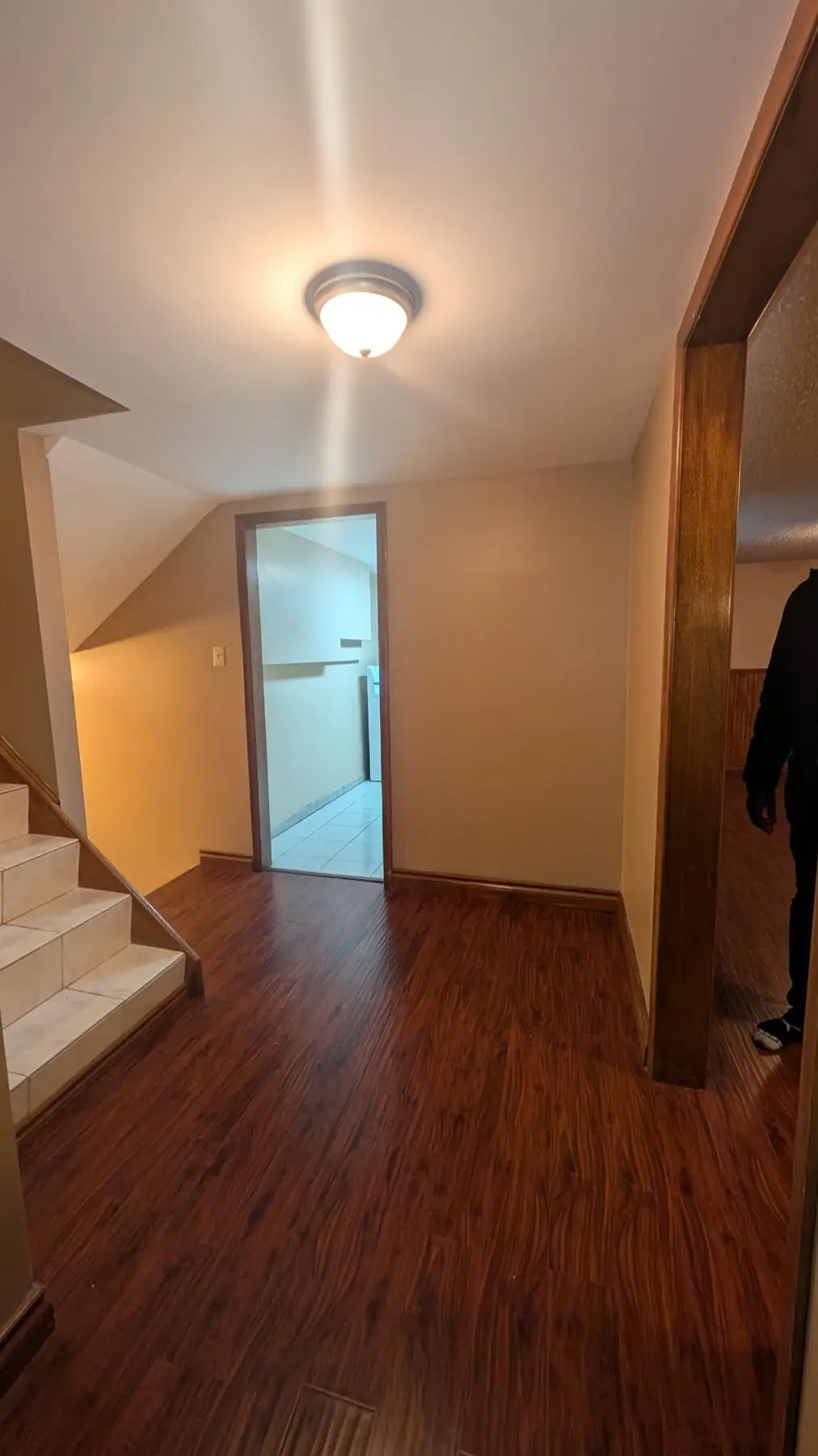 Finished — Basement hallway area with dark laminate flooring, tiled stairs, and doorway leading to another room.