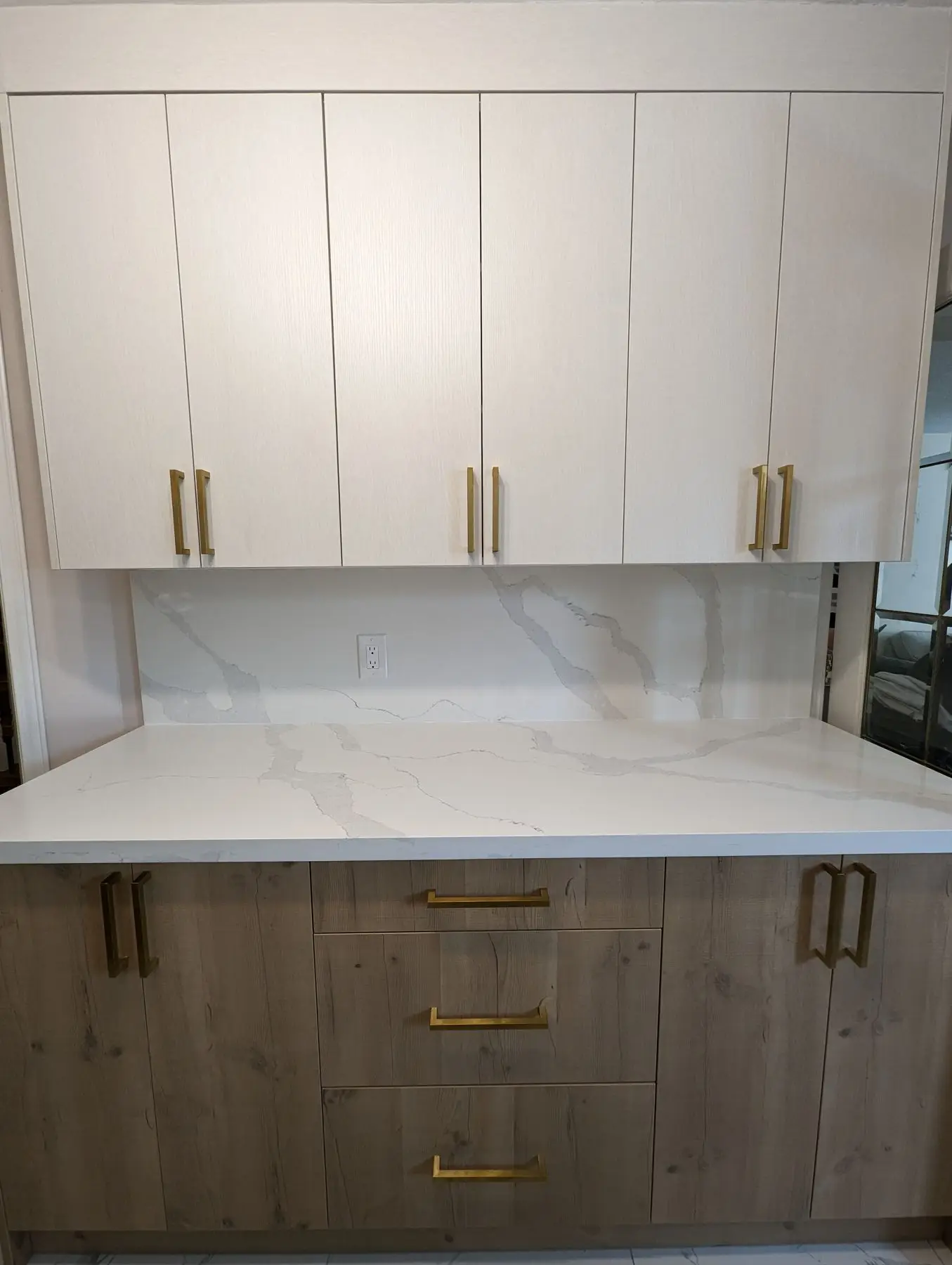 Finished — Completed kitchen feature wall with white upper cabinets, wood lower cabinets, quartz countertop, and gold hardware.